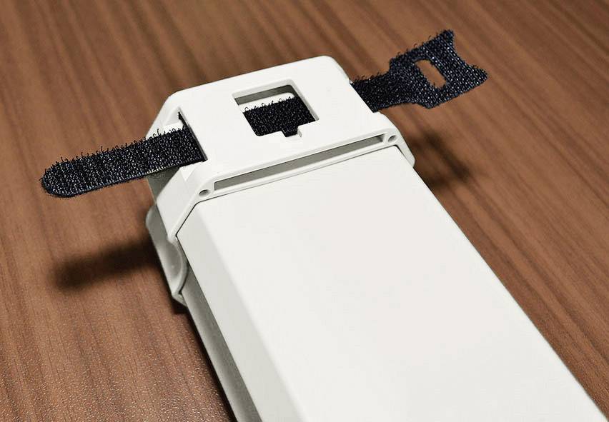 Ein rechteckiges, weißes Gerät mit schwarzen Klettverschlussbändern, das auf einer hölzernen Oberfläche liegt.