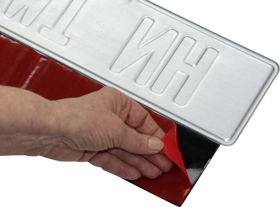 Eine Hand entfernt rote Schutzfolie von einer Metallplatte mit Prägung.