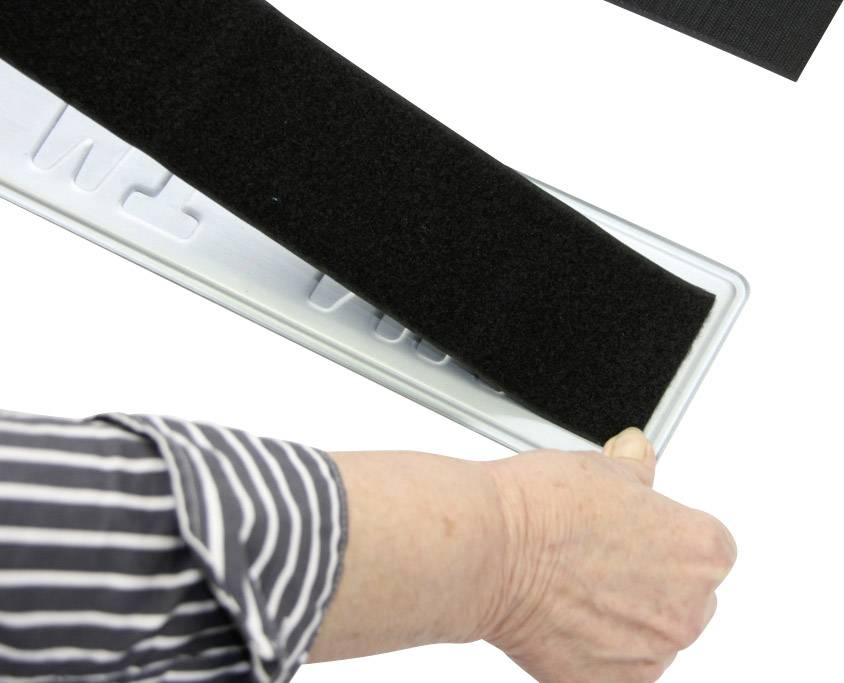 Eine Hand hält ein schwarzes Klettband über ein Nummernschild. Das Band kann zur Befestigung des Schildes genutzt werden.