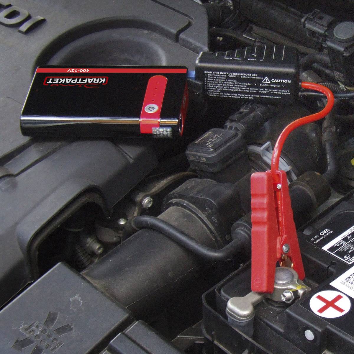 Ein schwarzes Auto-Batterie-Starthilfegerät ist am Motorraum eines Fahrzeugs angeschlossen, um die Batterie zu laden.