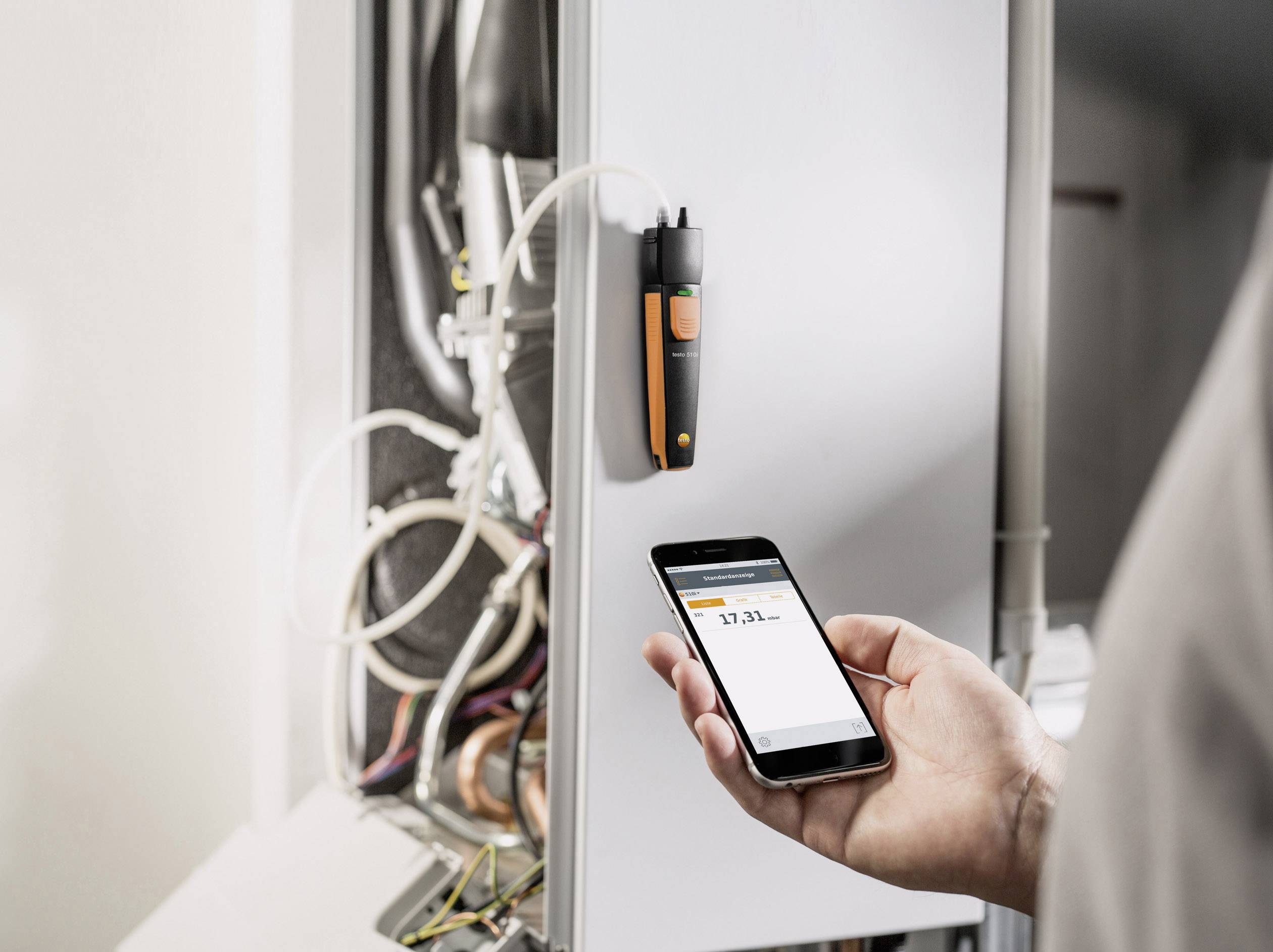 Eine Person misst mit einem Smartphone und einem angeschlossenen Sensor die Werte eines Heizkessels. Zahlen auf dem Bildschirm sichtbar.