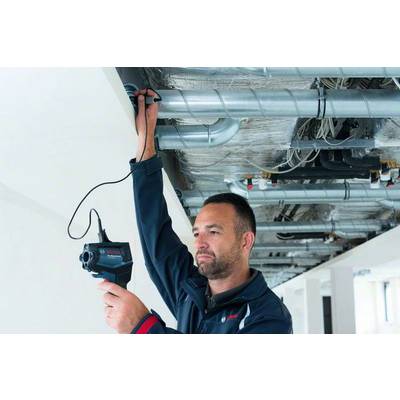 Eine Person überprüft mit einem Handgerät eine Klimaanlage an der Decke. Umgebung wirkt industriell oder in Bauarbeiten begriffen.