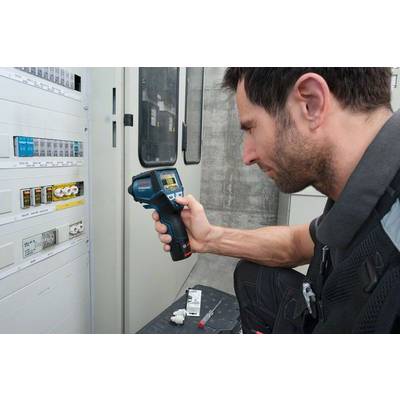 Ein Mann prüft mit einem Infrarotthermometer die Temperatur eines Sicherungskastens in einem Technikraum.
