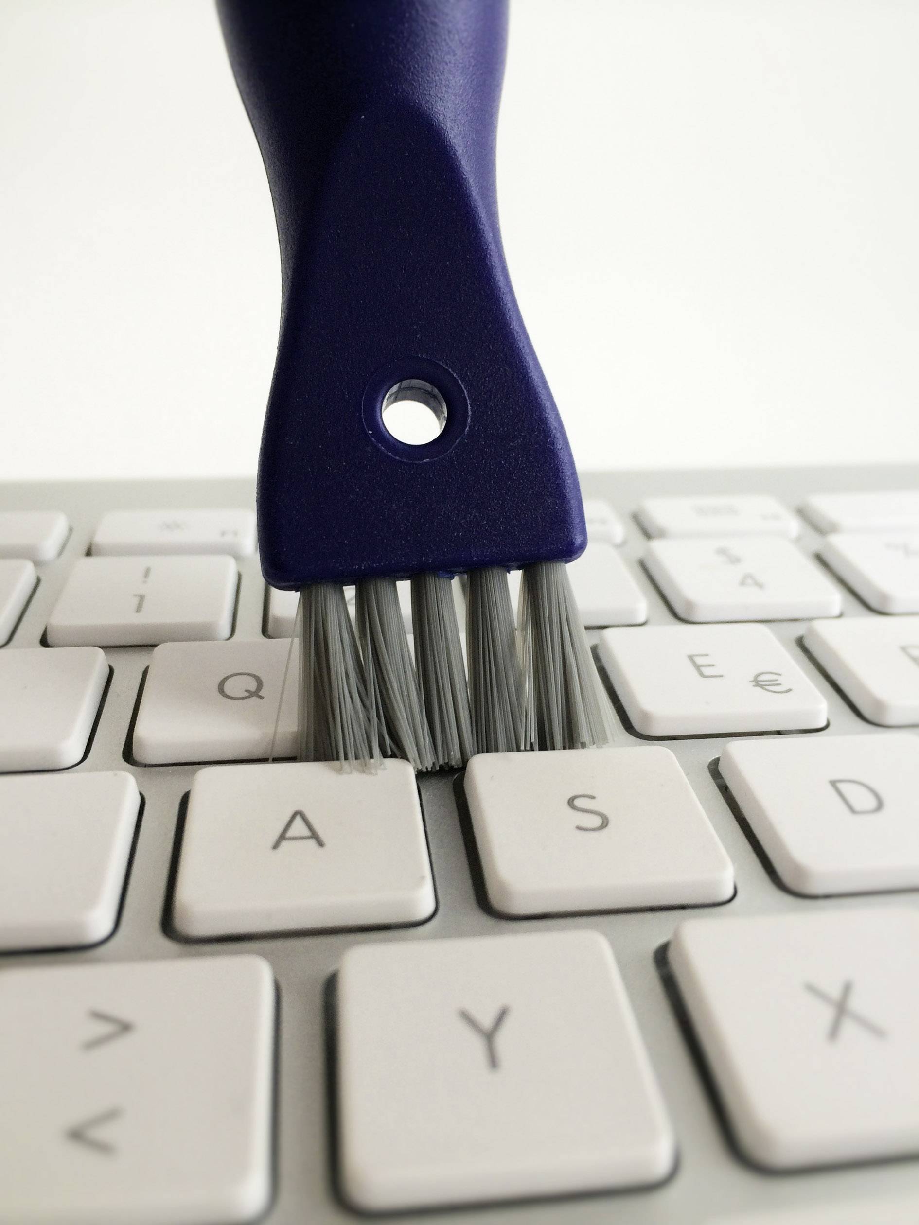 Eine Tastatur wird mit einer kleinen Bürste gereinigt. Die Bürste entfernt Staub zwischen den Tasten.