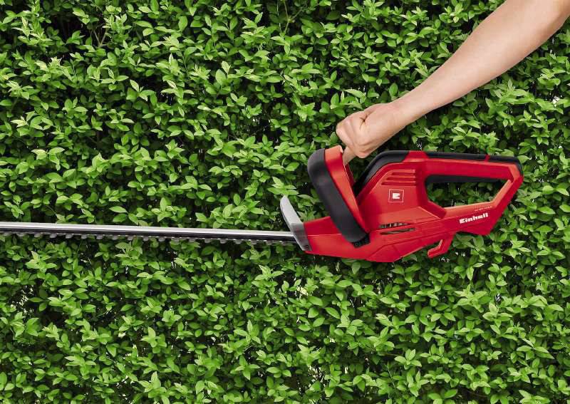 Eine Person schneidet eine grüne Hecke mit einer roten Elektroschere.