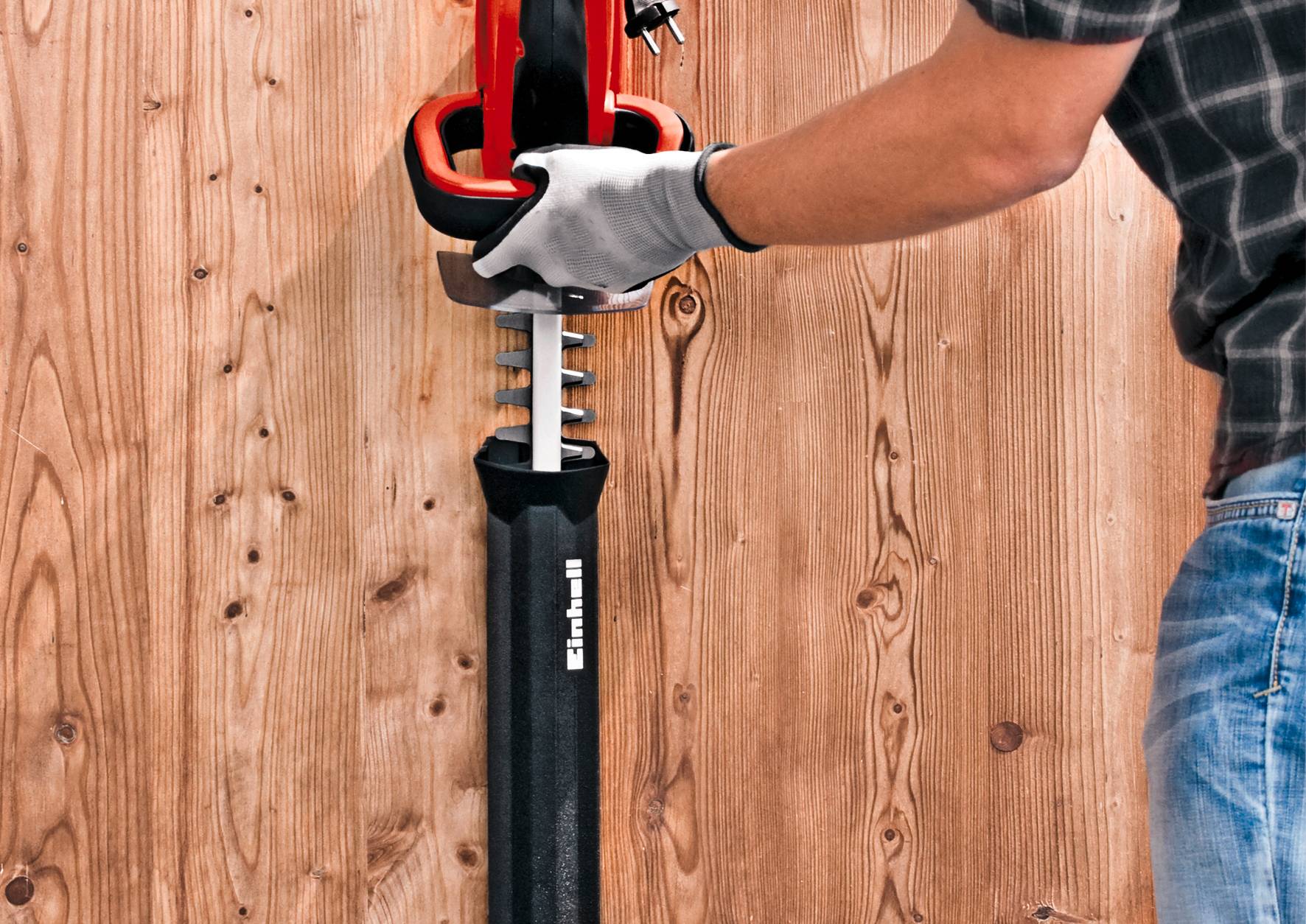 Eine Person benutzt eine rote Stichsäge, um in eine Holzplatte zu sägen. Die Säge hat einen schwarzen Griff, und die Person trägt Handschuhe.