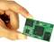 Eine Hand hält einen kleinen grünen Mikrochip mit mehreren Komponenten; er symbolisiert moderne Technologie und Miniaturisierung.
