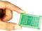 Eine Hand hält einen grünen Mikrochip mit sichtbaren Schaltungen und Anschlüssen. Der Chip ist klein und rechteckig.