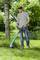 Ein Mann mäht Rasen mit einem elektrischen Trimmer im Garten. Im Hintergrund ist ein Baum und grüne Vegetation zu sehen.