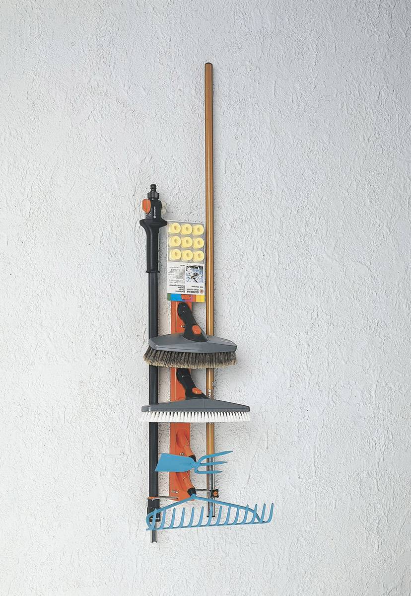 Ein Wandhalterungssystem mit Besen, Rechen und anderen Gartengeräten, ordentlich an einer weißen Wand organisiert.