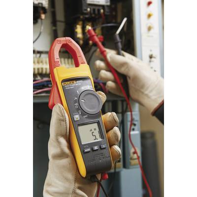 Eine Person hält ein Zangenmultimeter und misst den Stromfluss in einem Gerät, sichtbar ist eine Anzeige von 5,1 Ampere.