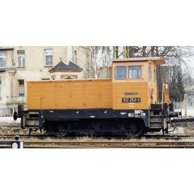 Eine orangefarbene Lokomotive steht auf einem Gleis vor alten Gebäuden. Aufschrift: 'Gleisbaufahrzeug' und '102 253-2'.