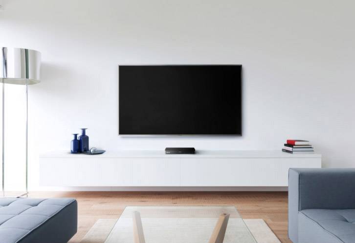 Ein modernes Wohnzimmer mit einem großen, an der Wand montierten Flachbildfernseher, einem weißen Sideboard und blauen Sofas.