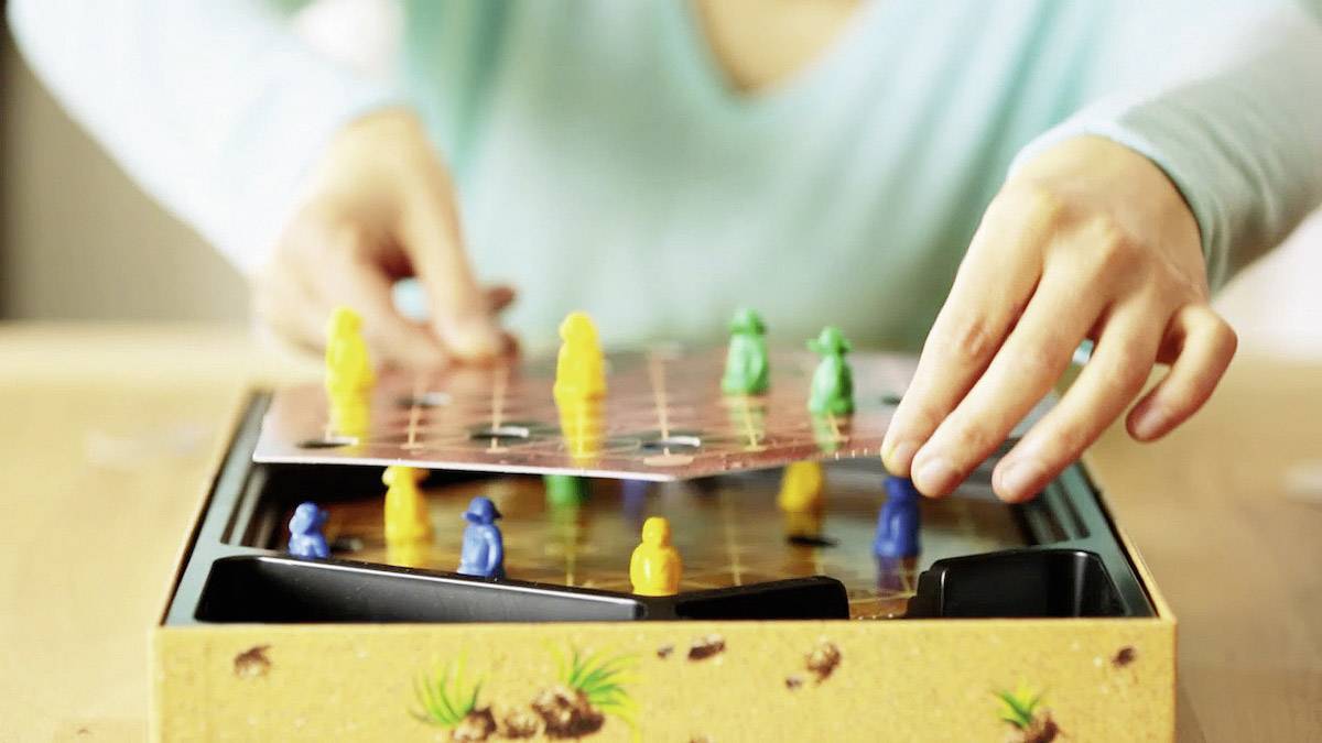 Eine Person legt eine Spielbrettabdeckung über ein Brettspiel, auf dem sich bunte Figuren befinden.