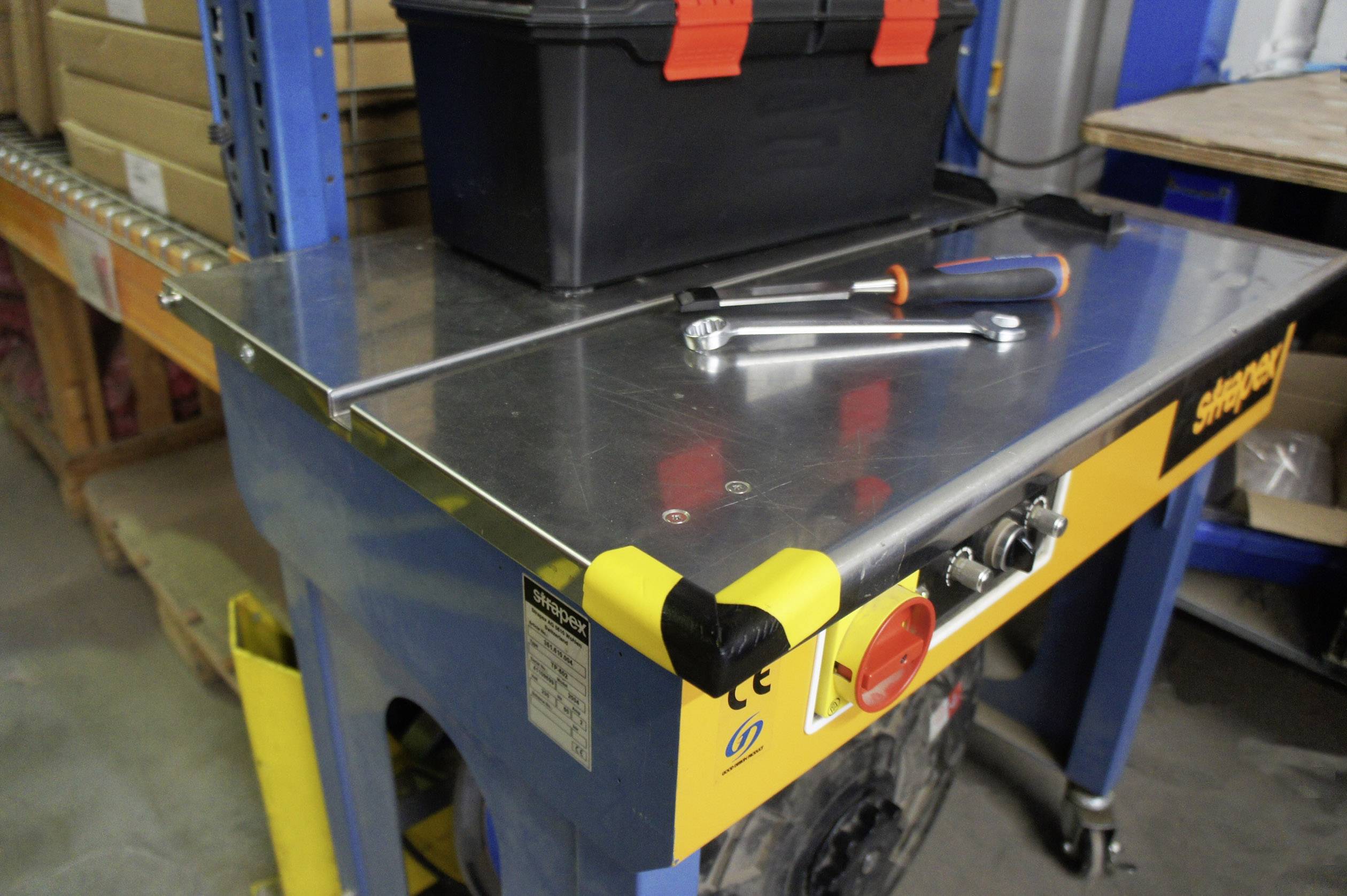 Arbeitstisch mit Metallschraubenziehern und einer schwarzen Werkzeugbox darauf, in einer Werkstatt mit Regalen im Hintergrund.