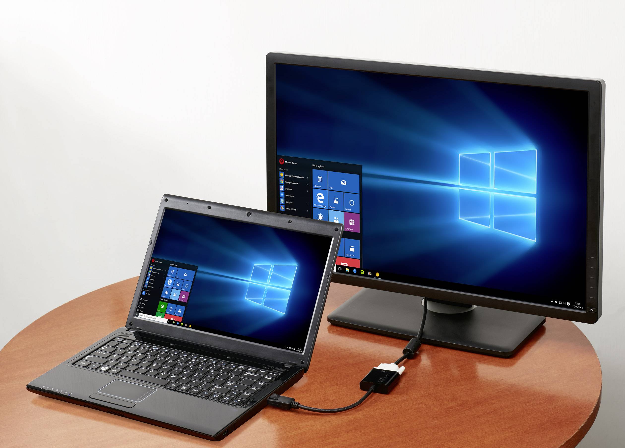 Ein Laptop ist über HDMI mit einem größeren Monitor verbunden, beide zeigen den Windows-Desktop mit geöffnetem Startmenü.