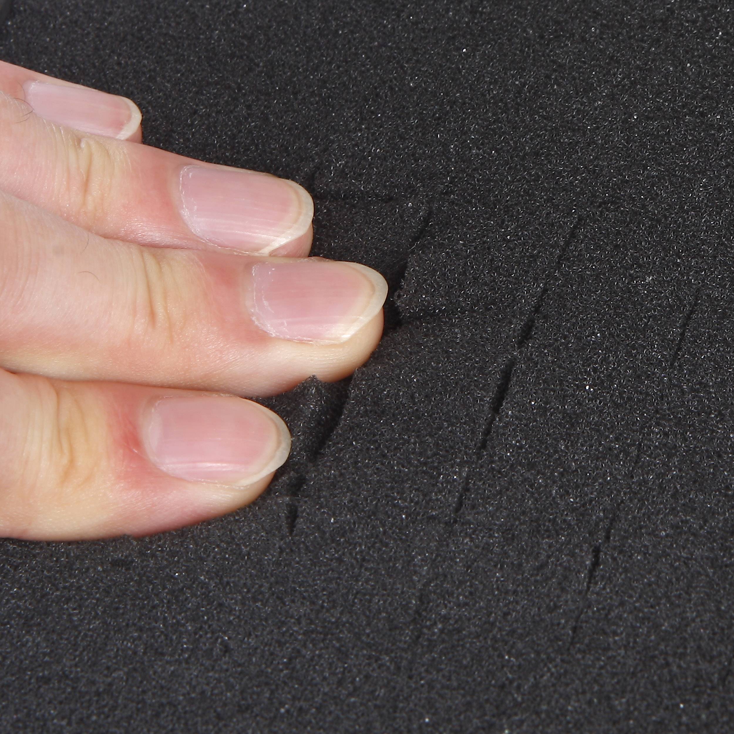 Eine Hand drückt auf schwarzen Schaumstoff, wodurch sichtbare Vertiefungen entstehen.