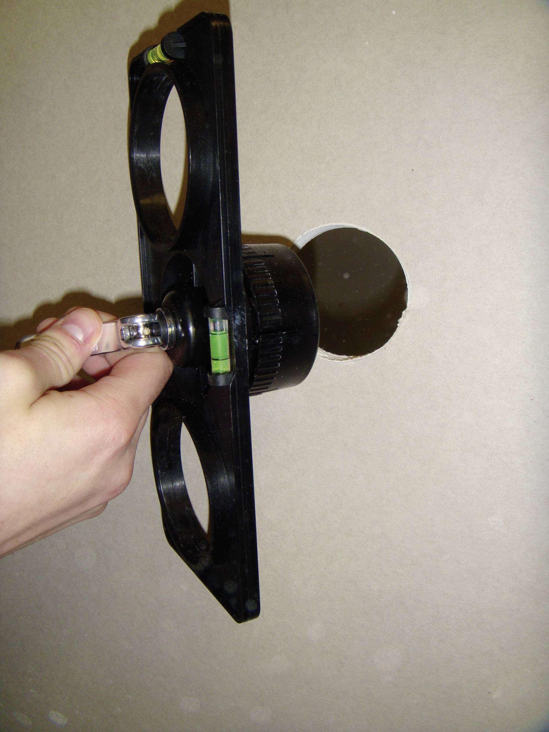 Eine Hand hält ein Bohrwerkzeug, das eine runde Öffnung in einer Wand durchbohrt.