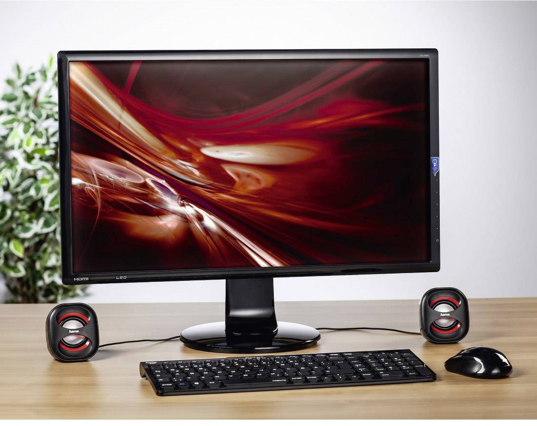 Monitor auf einem Schreibtisch, umgeben von Lautsprechern, Tastatur und Maus. Der Bildschirm zeigt ein abstraktes, rotes Muster.