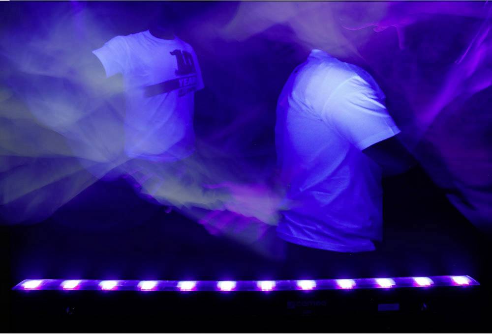 Zwei Personen in weißen T-Shirts unter UV-Licht. Bewegungsunschärfe und lila Schein, was eine dynamische Atmosphäre erzeugt.