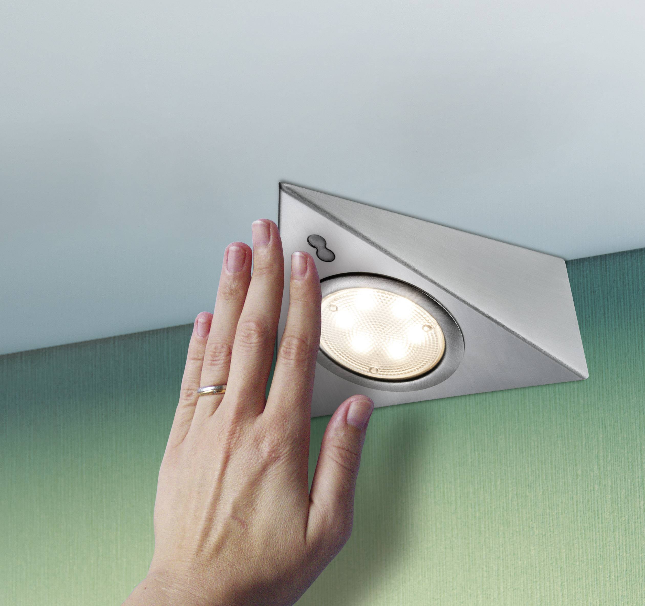 Hand schaltet LED-Deckenleuchte ein, montiert in dreieckigem Metallgehäuse an grüner Wand unter weißen Decke.