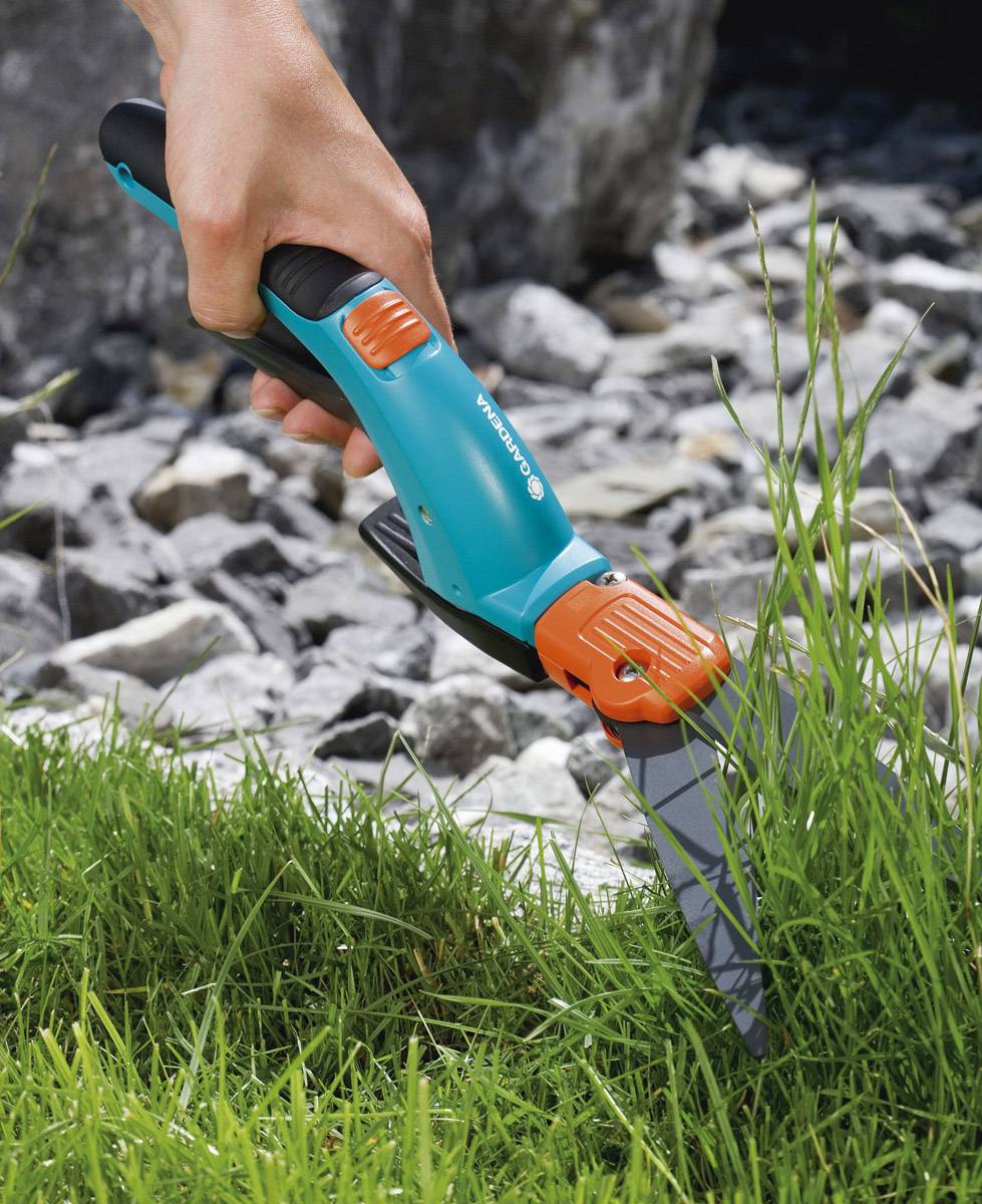 'Hand hält eine Gartenschere und schneidet Grasbüschel.'