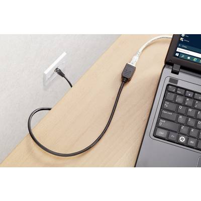 Ein Laptop auf einem Holztisch ist über ein schwarzes Kabel mit einer Steckdose an der Wand verbunden.