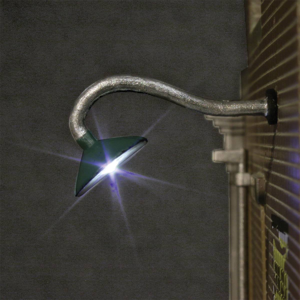 Eine grüne Bogenlampe an einer Backsteinwand leuchtet in der Dunkelheit.