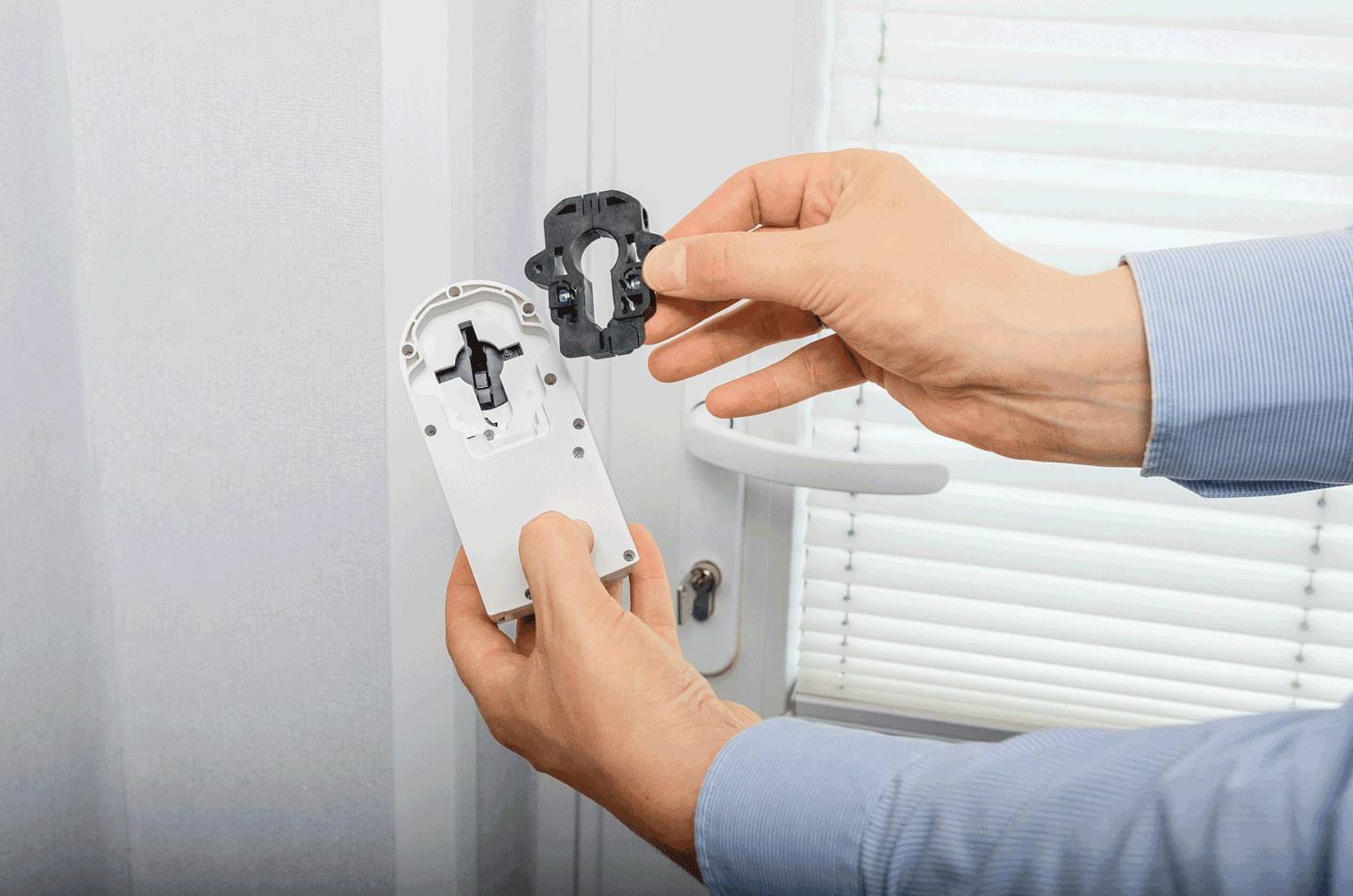 'Zwei Hände installieren ein elektronisches Schloss an einem Fenstergriff. Eine Abdeckung wird über der Mechanik angebracht.'