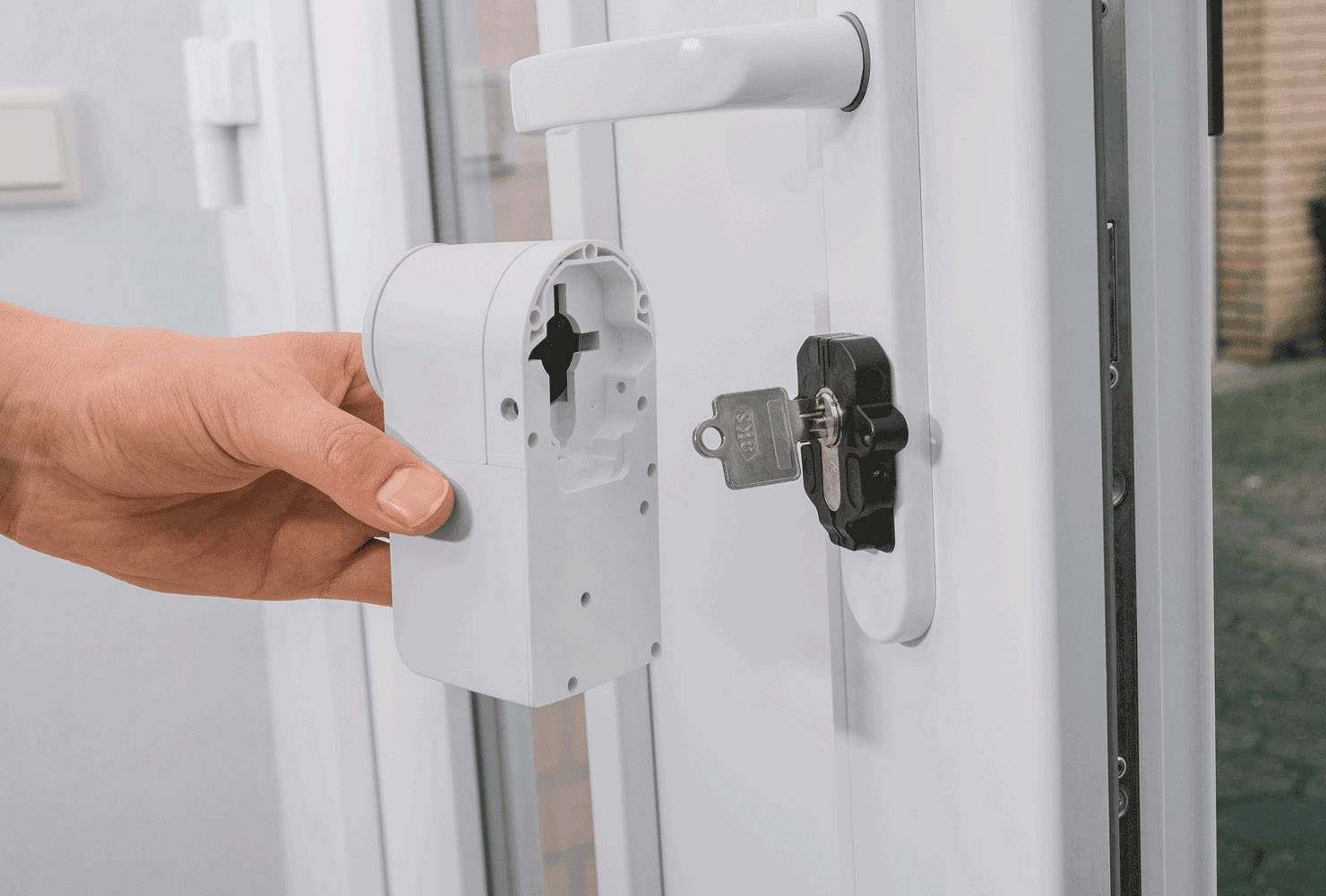 Eine Hand hält ein weißes elektronisches Türschloss, das zur Installation oder Entfernung von der Tür geöffnet ist. Ein Schlüssel steckt im Schloss.