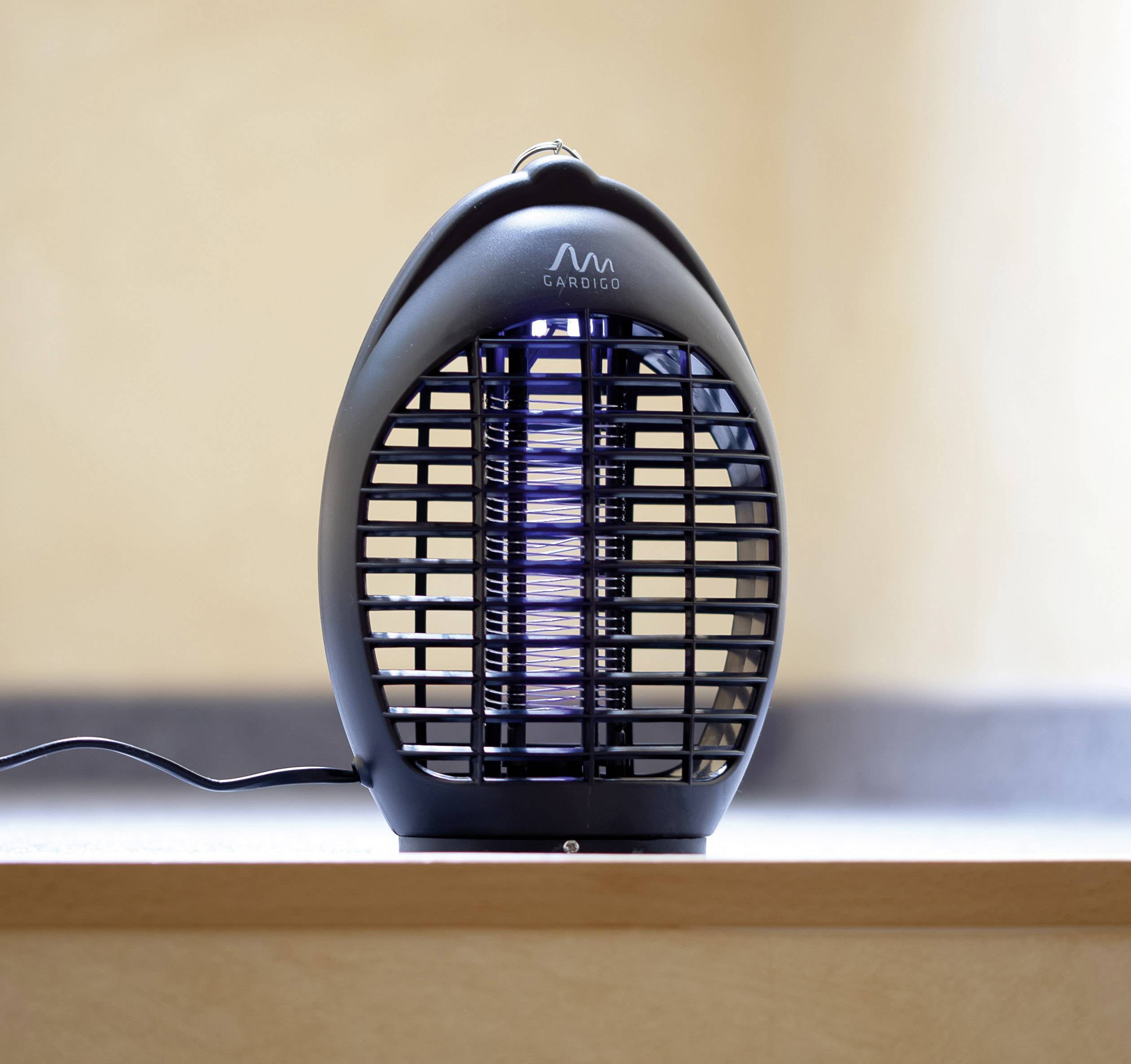 Ein elektronischer Insektenvernichter steht auf einem Tisch. Er hat ein schwarzes Gehäuse und ein Gitter, hinter dem das Licht sichtbar ist.