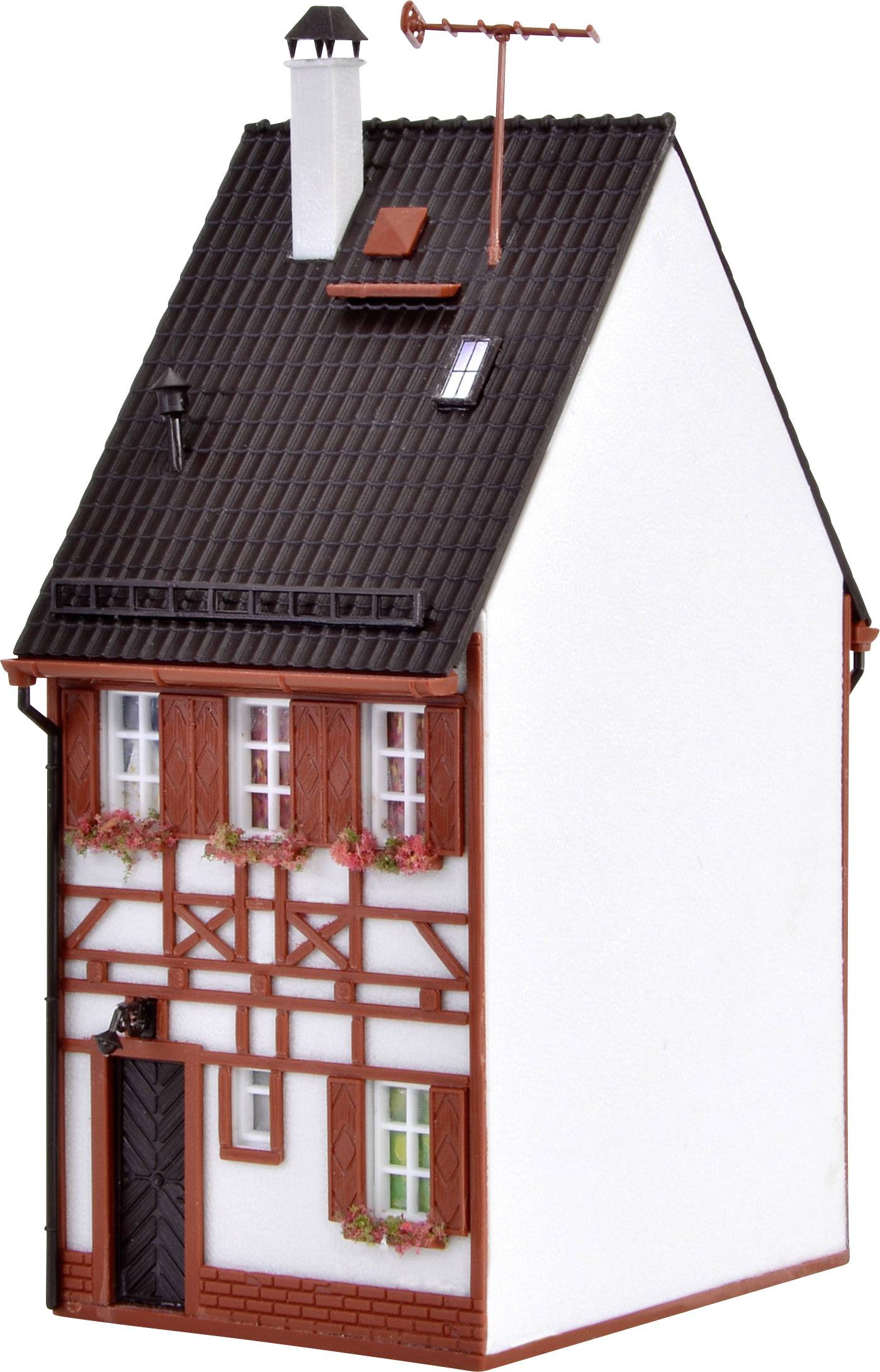 Ein kleines Modell eines Fachwerkhauses mit schwarzem Dach, rotem Fachwerk und weißen Wänden. Es hat Fenster mit Blumenkästen.