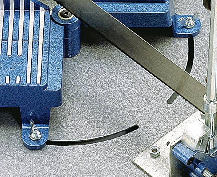 Industrielle Bandsäge schneidet Metallmaterial auf grauer Oberfläche. Zwei blaue Maschinenteile und Sägeblatt sind sichtbar.