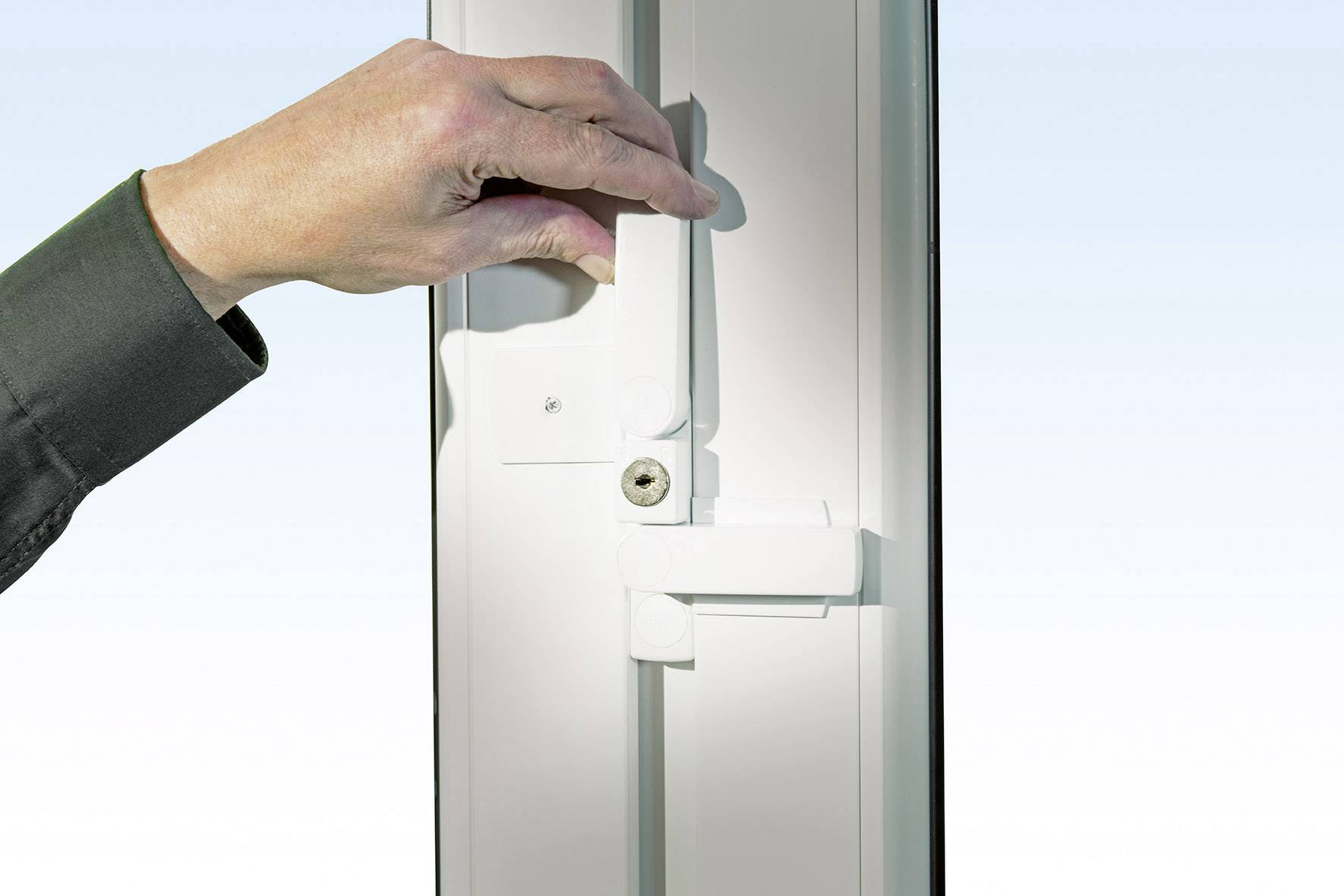 Eine Hand bewegt einen Fenstergriff nach oben, um das Fenster zu verriegeln. Der Hintergrund ist hellblau, das Fensterrahmen weiß.