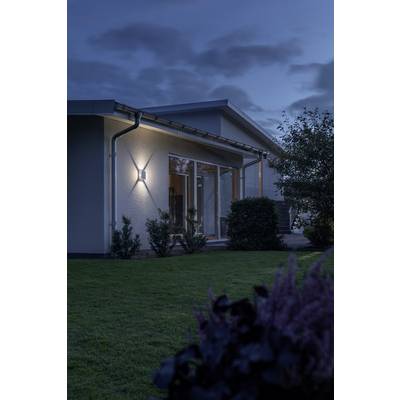 Ein modernes Haus mit Garten bei Dämmerung. Außenbeleuchtung erhellt die Hauswand, der Himmel ist wolkig, und Pflanzen umgeben das Gebäude.