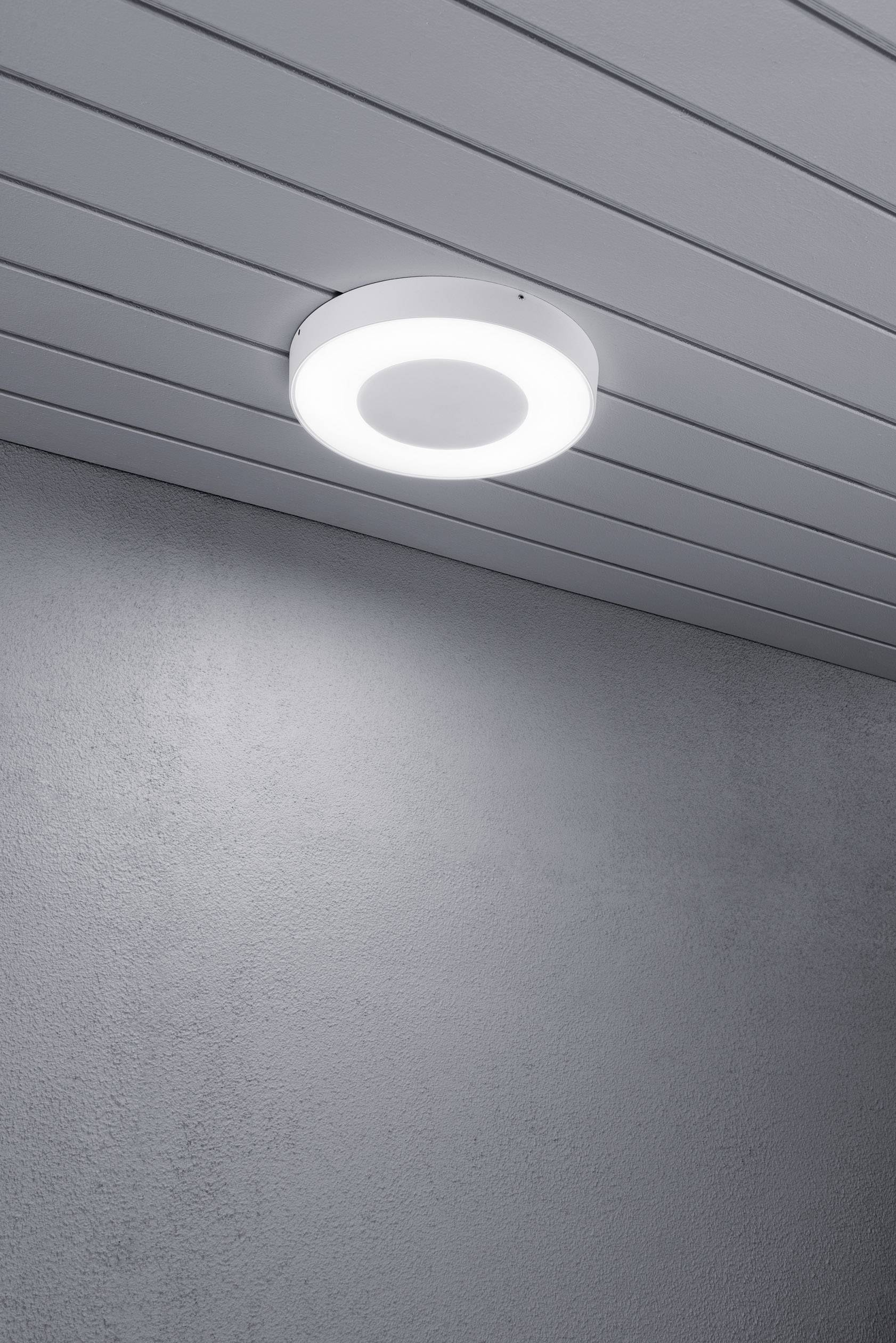 Eine runde, moderne Deckenleuchte mit einem gleichmäßigen, warmweißen Lichtschein an einer Holzdecke montiert, beleuchtet einen Raum.