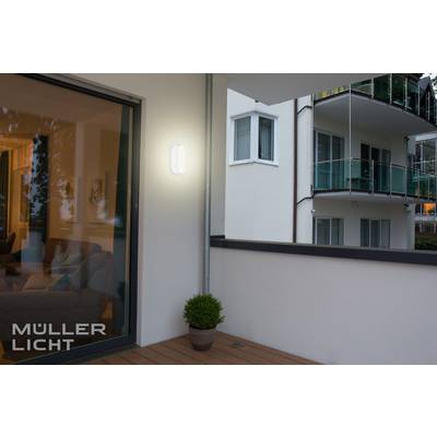 Ein beleuchteter Balkon bei Nacht mit einem hellen Licht an der Wand. Im Hintergrund ist ein modernes Wohnhaus mit Balkonen sichtbar.