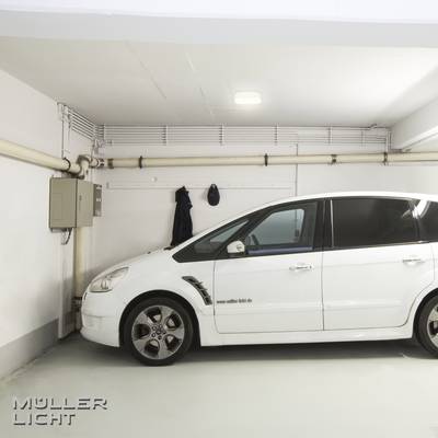 Ein weißes Auto parkt in einer Garage. An der Wand hängen Rohre und ein Sicherungskasten. Unten links steht 'Müller Licht'.