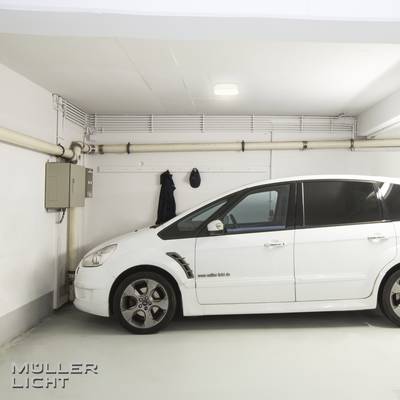 Ein Auto steht in einer hell erleuchteten Garage. An den Wänden sind Rohrleitungen und ein Stromkasten zu sehen.