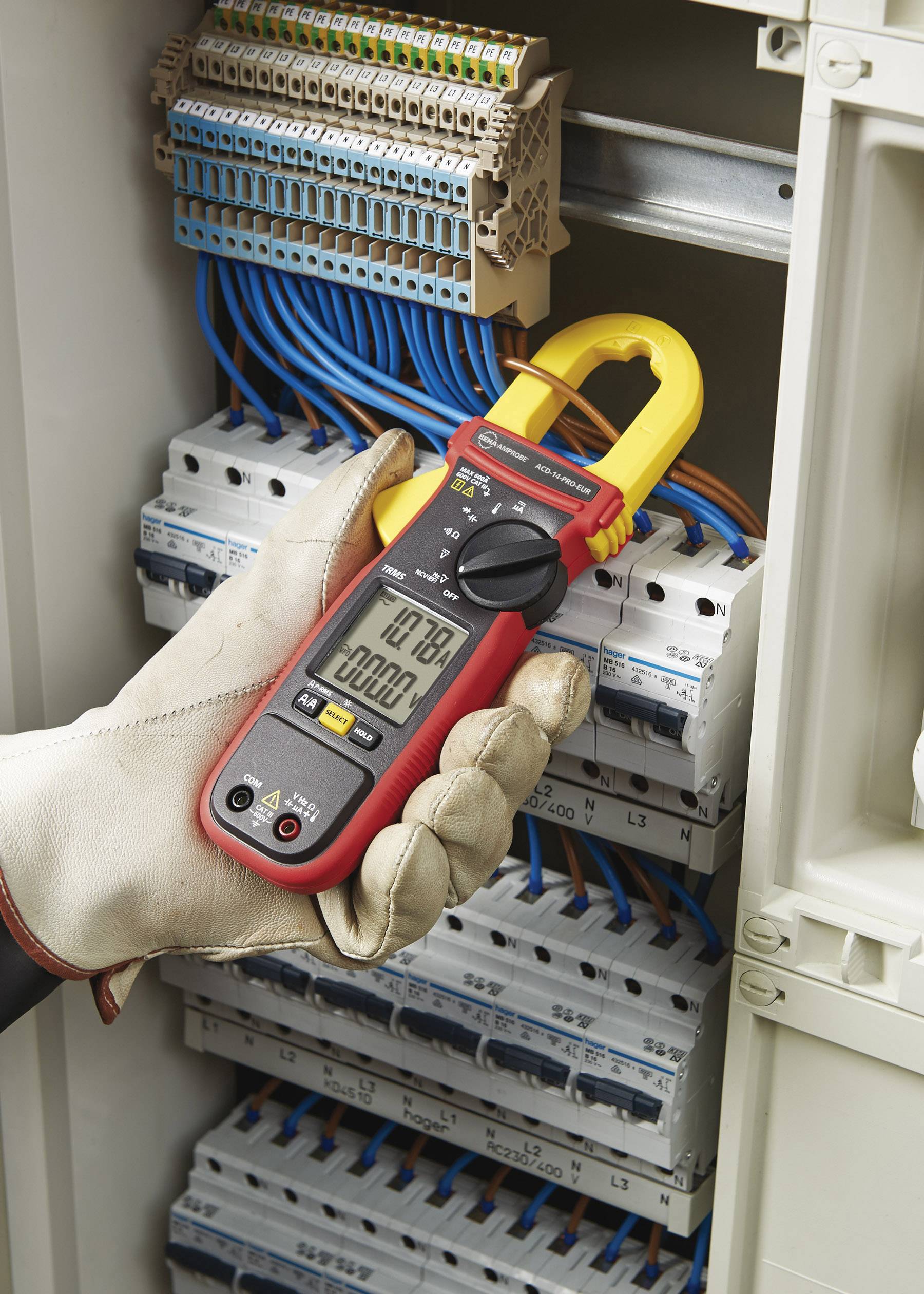 Eine behandschuhte Hand hält ein Multimeter, das an einem elektrischen Schaltschrank mit blauen Drähten Messungen durchführt.