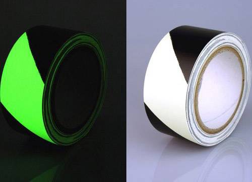 Eine Rolle schwarz-weißes Klebeband; links leuchtet der weiße Teil grün im Dunkeln, rechts erscheint er weiß im Licht.