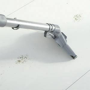 Ein grauer Staubsaugeraufsatz reinigt eine weiße, geflieste Fläche mit sichtbaren Schmutzflecken.