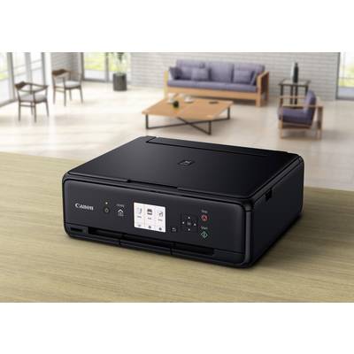 Ein schwarzer Drucker steht auf einem Tisch in einem modernen Wohnzimmer. Im Hintergrund sind ein Sofa und ein Couchtisch zu sehen.