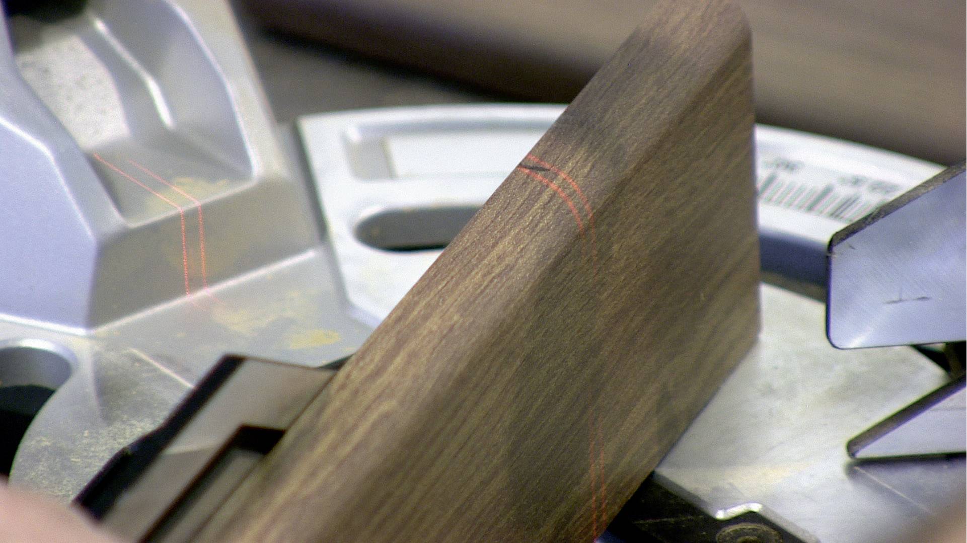 Nahaufnahme eines Stücks Holz auf einer Gehrungssäge, mit einem gut sichtbaren roten Laser, der die Schnittlinie markiert.