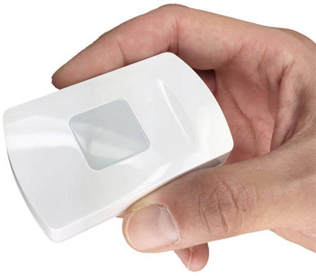 Hand hält einen kleinen, weißen rechteckigen Sensor mit einer glatten Oberfläche und einer quadratischen Erhebung in der Mitte.