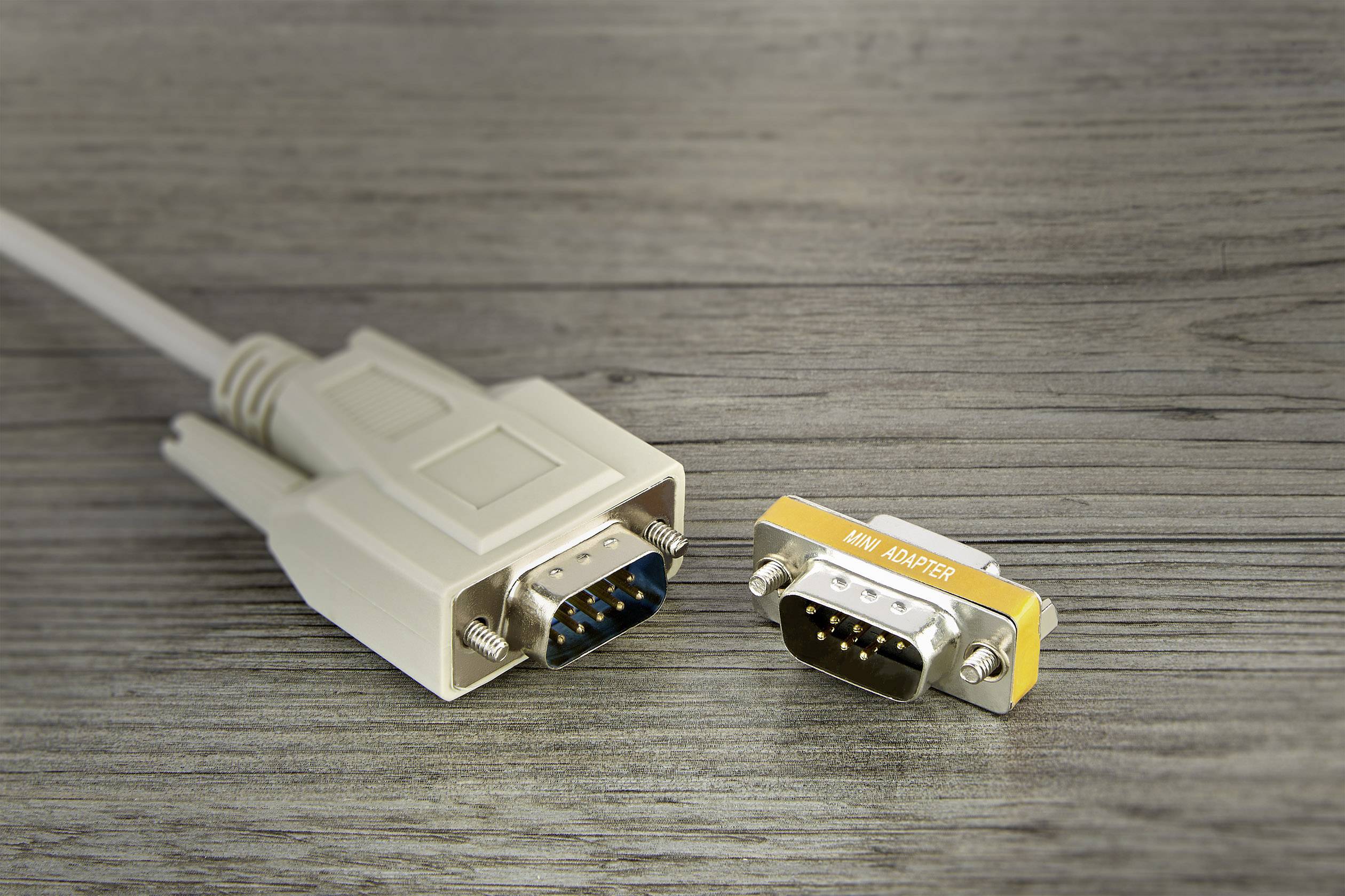 'VGA-Kabel mit 9-poligem Stecker neben einem 9-poligen Mini-Adapter auf einem Holztisch'