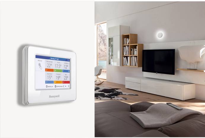 An der Wand ist das zentrale Bediengerät des Honeywell evohome Systems angebracht. Dahinter eröffnet sich der Blick aufs gemütlich eingerichtete Wohnzimmer mit Couch, Sideboard, Fenster und Bücherregal