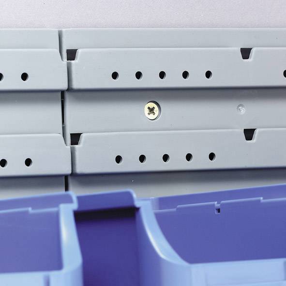 Graue Plastikwand mit Schrauben und blauen Aufbewahrungsbehältern im unteren Bereich. Fokus auf Montage- und Befestigungsdetails.