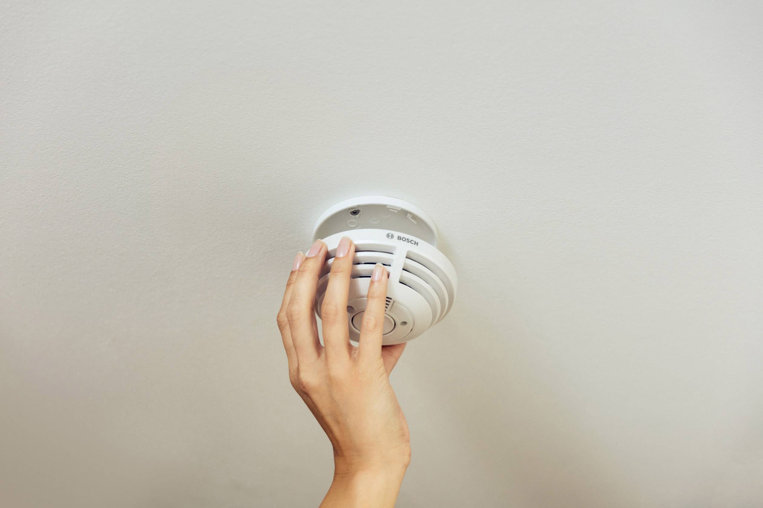 Eine Hand überprüft einen an der Decke montierten Rauchmelder, um die Funktionalität zu gewährleisten und die Sicherheit zu erhöhen.