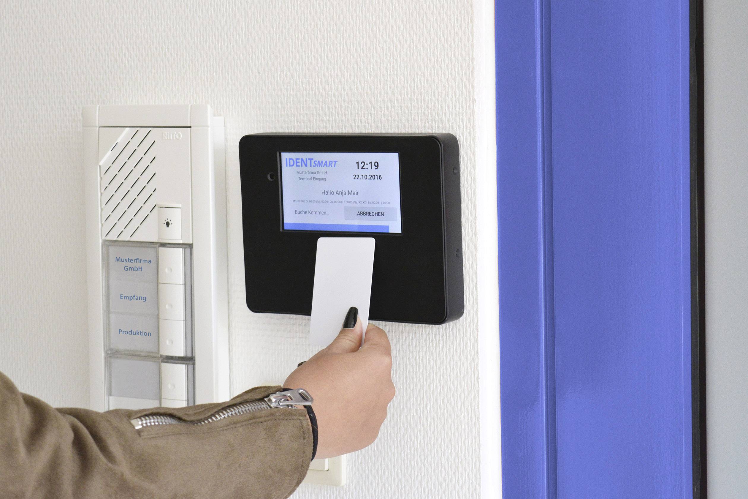 Das Bild zeigt, wie eine NFC-Karte zur Arbeitszeitbuchung an ein an der Wand montiertes Lesegerät  gehalten wird. 